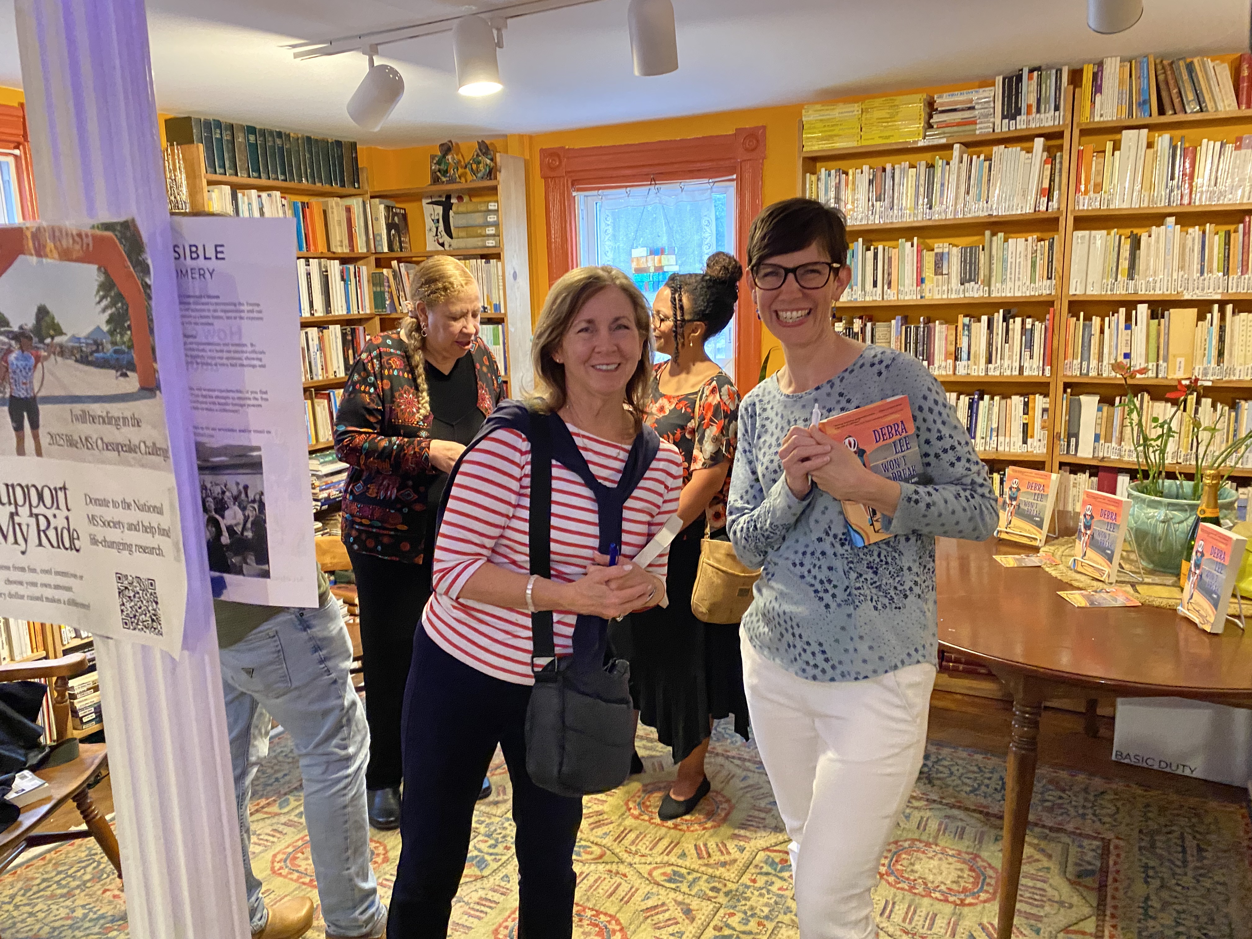 Two women standing in front of a brown table with books behind them