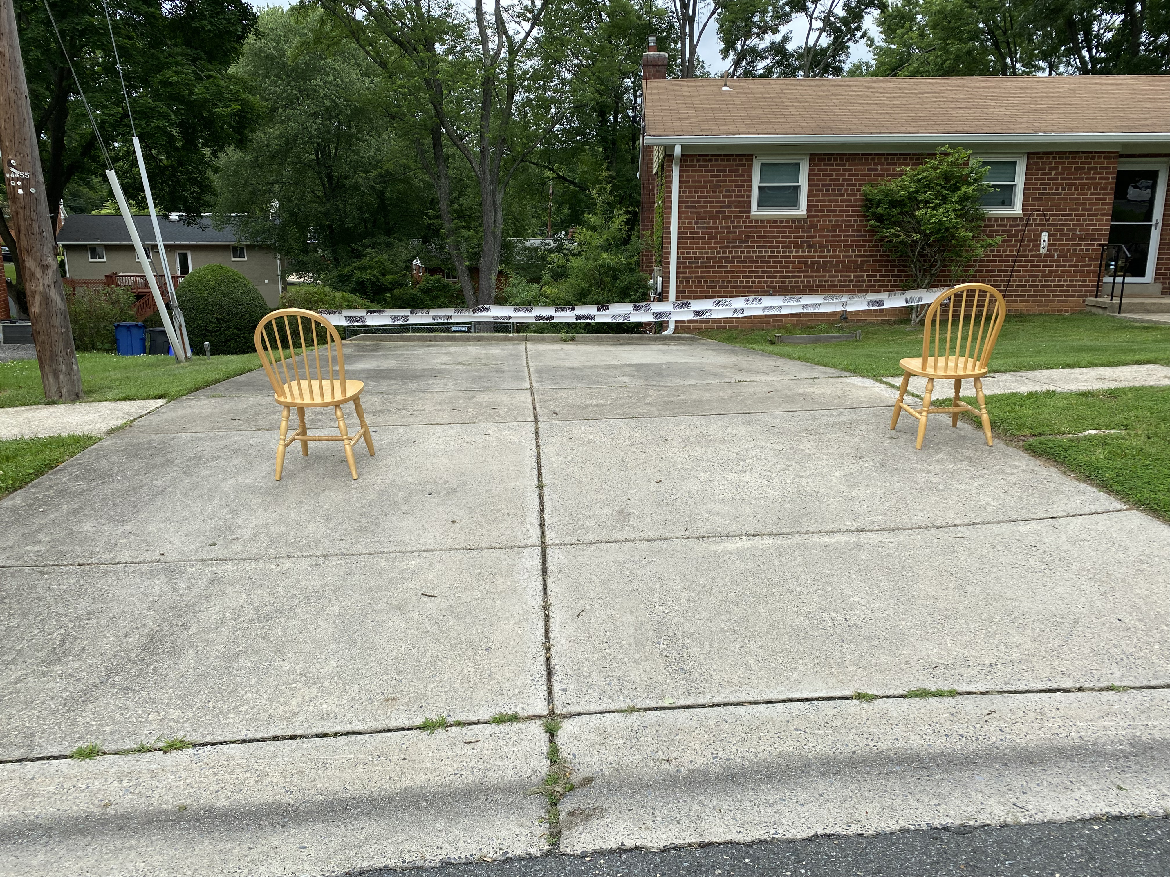 Photo of two wooden chairs on a driveway with a black-and-white streamer tied between them across the width of the driveway