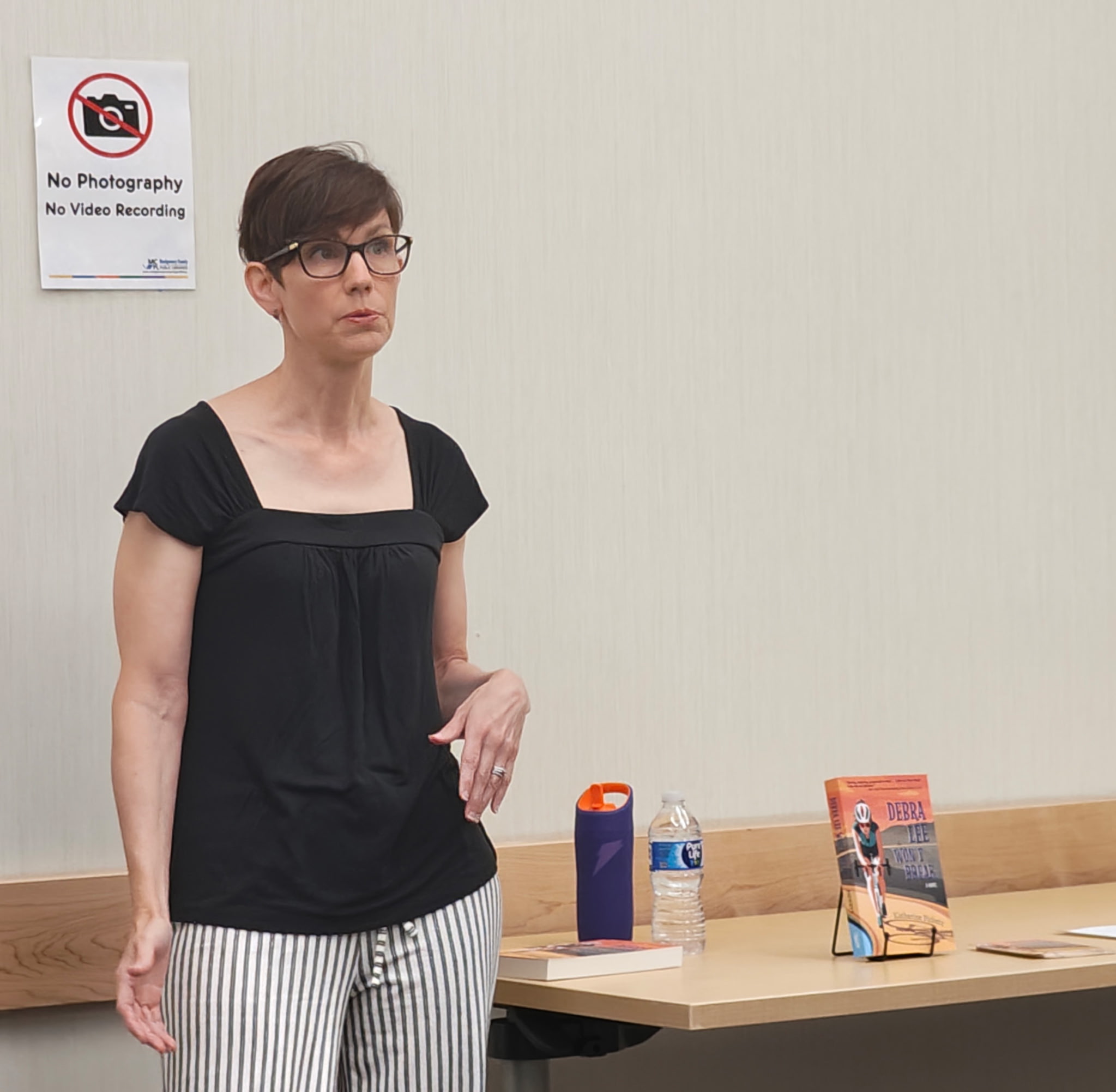 Photo of a white woman wearing a black shirt and black-and-white striped pants standing next to a table