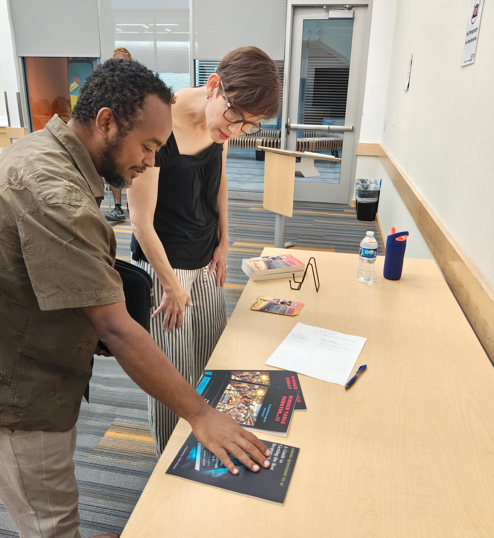 A woman and man stand next to each other in front of a table looking at several books